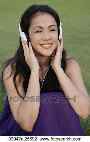 Portrait of young woman listening to music at park View Large Photo Image Stock Image - Portrait of young woman listening to music at park. Fotosearch