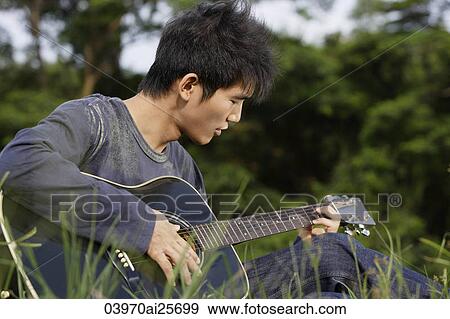 Young man playing guitar in grass View Large Photo Image Stock Photo - Young man playing guitar in grass. Fotosearch