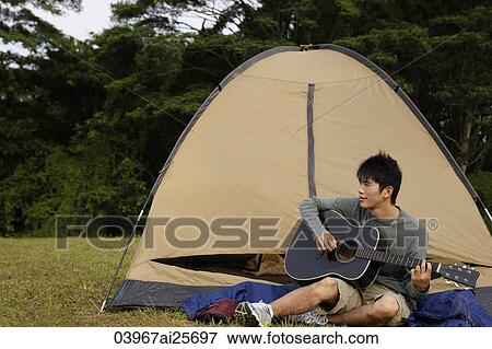 Young man playing guitar outside of tent View Large Photo Image Stock Photo - Young man playing guitar outside of tent. Fotosearch