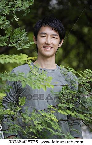 Stock Photography - Young man smiling behind foliage. Fotosearch