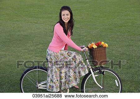 Stock Photo - Young woman riding bike with basket full of flowers. Fotosearch