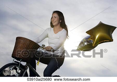 Stock Image - Young woman riding bike with star-shaped balloons. Fotosearch