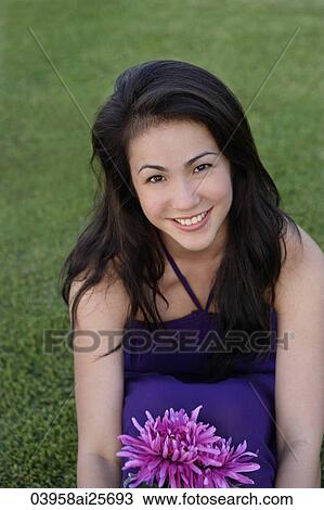 Young woman sitting on grass holding flowers View Large Photo Image Stock Image - Young woman sitting on grass holding flowers. Fotosearch