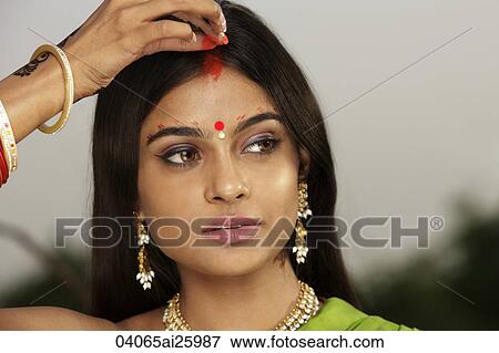 Stock Photo - woman wearing sari, applying Sindoor powder down her hair part. Fotosearch