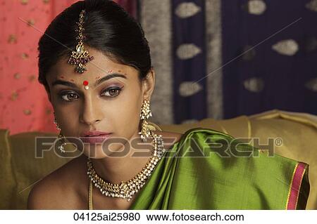 Stock Image - woman wearing sari, surrounded by sari fabric, decorated with henna tattoos, jewelry and bindi. Fotosearch