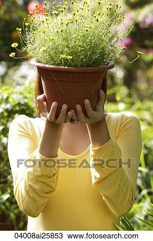 Stock Image - Young woman at nursery, holding potted plant. Fotosearch