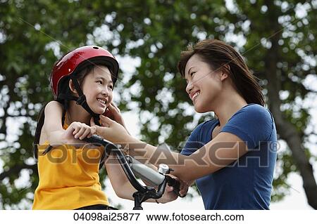 Stock Photo - Young woman fastening bike helmet on girl. Fotosearch