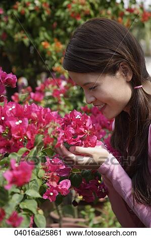 Stock Image - Young woman holding up flowers to smell. Fotosearch