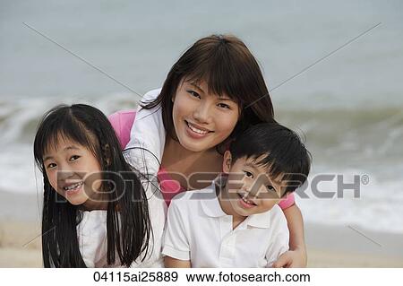Stock Photo - Young woman hugging boy and girl on beach. Fotosearch