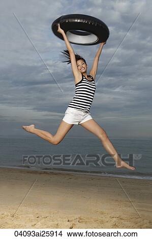 Young woman jumping on beach, holding up inner tube View Large Photo Image Picture - Young woman jumping on beach, holding up inner tube. Fotosearch