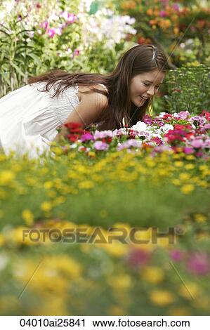 Stock Image - Young woman leaning over to smell the flowers. Fotosearch