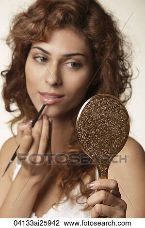Stock Image - Young woman painting her lips. Fotosearch