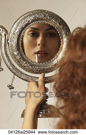Picture - Young woman painting her lips, using hand mirror. Fotosearch