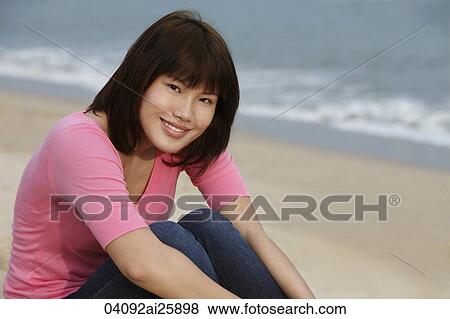 Stock Photo - Young woman sitting on beach. Fotosearch