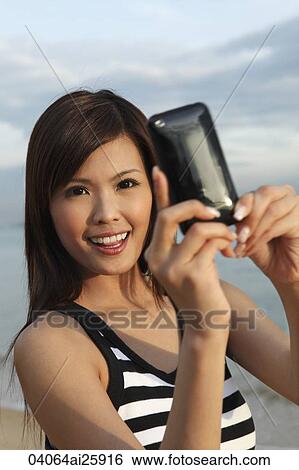 Stock Photograph - Young woman taking photo with camera phone. Fotosearch