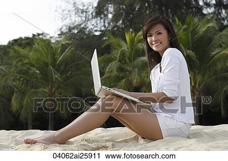 Stock Image - Young woman working on laptop on beach. Fotosearch