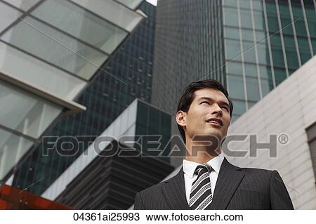 Stock Image - business man in suit standing among tall buildings. Fotosearch