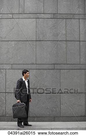 Stock Photography - businessman holding briefcase and wearing backpack. Fotosearch