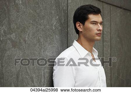 Stock Photo - man in white shirt leaning against wall. Fotosearch