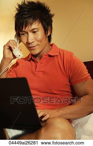 Stock Image - man talking on phone while on laptop. Fotosearch