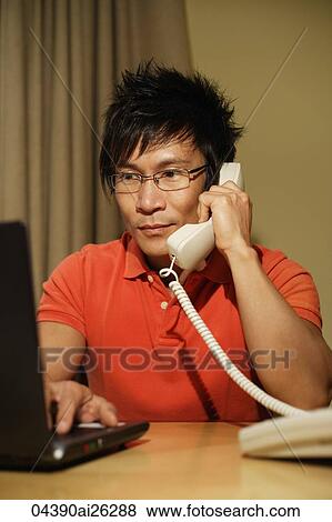 Stock Photo - man working at laptop while on phone. Fotosearch