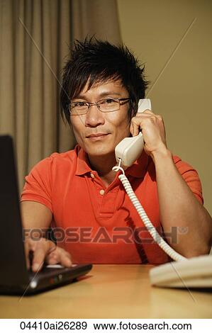 Stock Photo - man working on laptop while on phone. Fotosearch