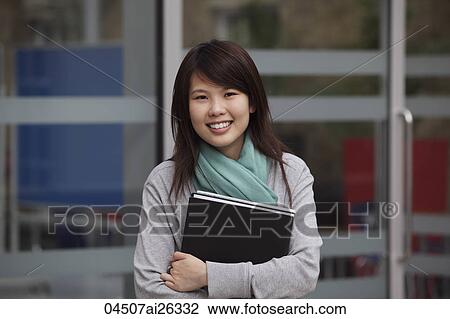 Stock Image - Chinese woman holding a folder in front of a University.. Fotosearch