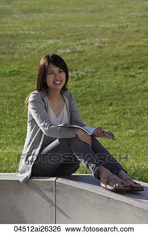 Stock Photograph - Chinese woman sitting by grass reading a book.. Fotosearch