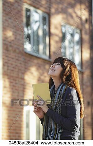 Asian woman holding a book looking up, smiling View Large Photo Image Picture - Asian woman holding a book looking up, smiling. Fotosearch