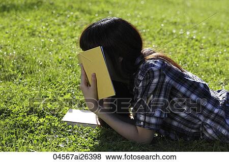 Stock Photo - Asian woman laying on grass hiding face with a book.. Fotosearch