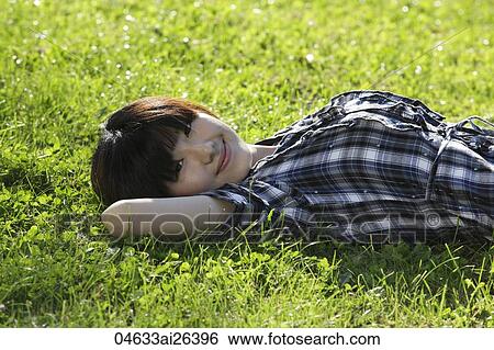 Stock Photograph - Asian woman laying on grass smiling.. Fotosearch