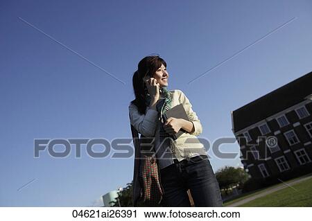 Stock Image - Asian woman smiling and talking on phone outside.. Fotosearch
