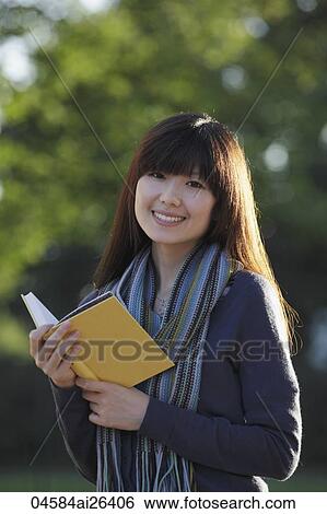 Stock Photograph - Asian woman smiling, holding book.. Fotosearch