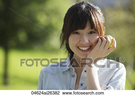 Asian woman smiling while holding apple, outdoors. View Large Photo Image Stock Image - Asian woman smiling while holding apple, outdoors.. Fotosearch