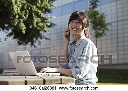 Asian woman talking on phone while working on laptop, outside. View Large Photo Image Stock Image - Asian woman talking on phone while working on laptop, outside.. Fotosearch