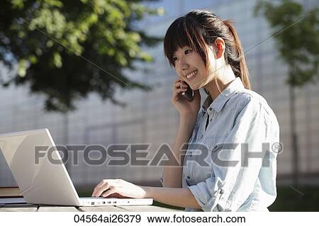 Asian woman working on laptop and talking on phone, outside. View Large Photo Image Stock Photo - Asian woman working on laptop and talking on phone, outside.. Fotosearch