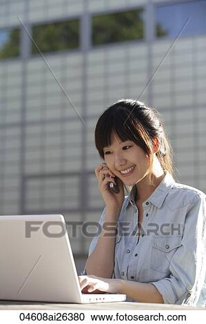Asian woman working on laptop while talking on phone, outside. View Large Photo Image Stock Image - Asian woman working on laptop while talking on phone, outside.. Fotosearch