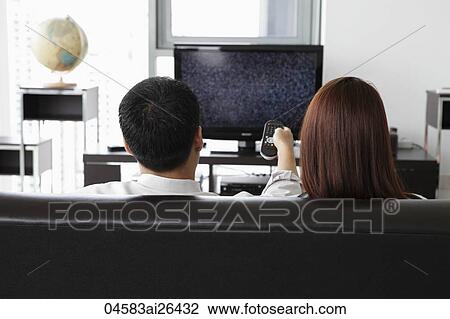 Stock Image - Back view of young couple watching TV at home. Fotosearch
