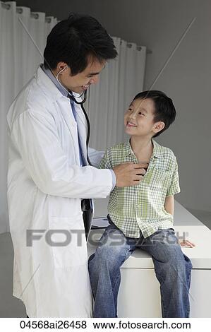 Doctor listening to young boy's heart and smiling at eachother View Large Photo Image Stock Photo - Doctor listening to young boy's heart and smiling at eachother. Fotosearch