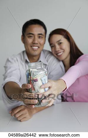Young couple holding jar of money View Large Photo Image Stock Image - Young couple holding jar of money. Fotosearch
