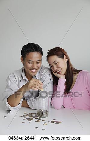 Stock Image - Young couple saving money in a jar. Fotosearch