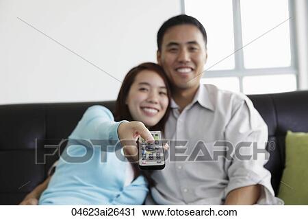 Stock Image - Young couple watching TV and smiling. Fotosearch