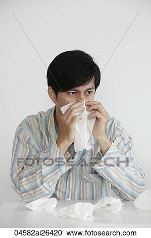 Stock Image - young man blowing his nose with tissue. Fotosearch