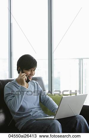 Stock Image - Young man talking on phone and working on laptop. Fotosearch