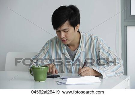 Stock Photo - Young man working on bills at home. Fotosearch