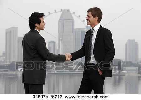 Stock Photo - Chinese and Caucasian man shaking hands in front of skyline. Fotosearch