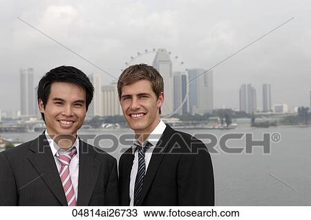 Stock Image - Chinese and Caucasian man standing in front of city skyline. Fotosearch