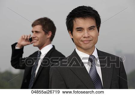 Stock Photo - Chinese business man in foreground, Caucasian man on phone in background. Fotosearch