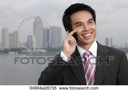 Stock Photography - Chinese business man talking on phone in front of city skyline. Fotosearch