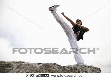 Stock Image - Chinese man doing a high kick on top of rock. Fotosearch